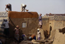 Group of women preparing house front for decorative painting in traditional Gourounsi village.