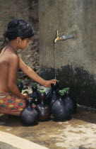 Mrong girl fetching water from outside tap in small flasks.