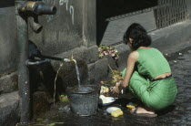 Young woman using tap in street to wash dishes in the market.Burma Myanmar Rangoon