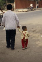 Man holding the hand of a little boy wearing seatless trousers to save wearing nappies.