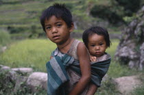 Portrait of fugao children with one child carrying a younger child in a sling on his back in rural area