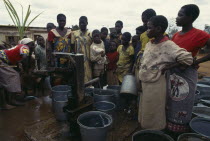 Women and children crowded around water pump with buckets.