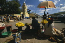 The Square.  Market with women selling fruit from stall in the foreground.