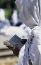 Woman in white head covering reading from book during ceremony at St George Church  Kidus Giorgis.