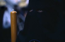 Semana Santa Easter procession. Penitent in black robe with eyes visable through hood holding a candle