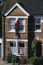 Window cleaner on ladder cleaning outside of household windows.Washing