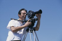Male film cameraman with old style camera on tripod