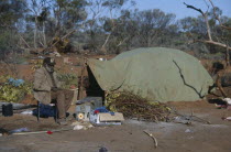 Aboriginal man sat on a chair next to a green tent in an Aborigine camp