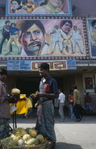 Cinema with colourful poster hoadings above entrance and men at a fruit stall in the foreground