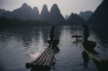 Cormorant fishermen silhouetted on stretch of river in the Guilin area with limestone peaks behind.