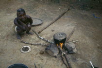 Woman cooking on open fire with cooking pot balanced on stones.