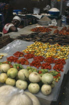 Display of vegetables and fish for sale in the covered market with female vendor leaning on table top.Cte d Ivoire