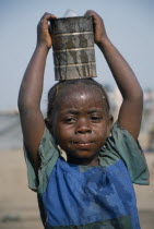 Little girl with braided hair at camp for refugees from Sierra Leone carrying can of water on her head.