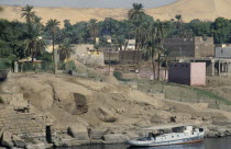 Oldest inhabited part of Aswan  flat roof houses amongst palm trees and boat moored against shore.