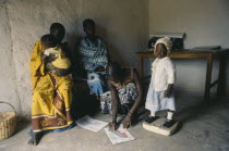 Nurse in rural area weighing child and making notes on growth chart.