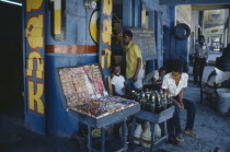 Children and young men outside shop of sweets and drinks vendor with blue and yellow painted exterior.Ayiti Caribbean Haitian Kids Store West Indies Latin America Latino American Immature Male Man Guy
