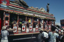 Brightly painted and crowded taptap bus with waiting crowds and food sellers.