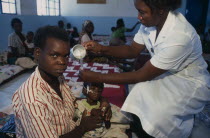 Nurse feeding child through tube in day feeding centre for malnourished children in camp for Angolan refugees. Center
