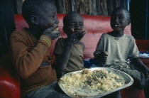 Three young children using right hands to eat Christmas lunch.East AfricaThesigers