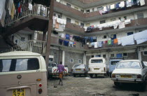 Middle class housing close to slum area with washing hanging from balconies of four storey buildings and parked cars and person in courtyard in foreground.East Africa