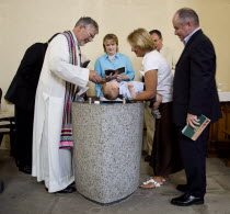 Baby having holy water poured over head during baptism ceremony.    Priest Vicar