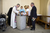 Baby having holy water poured over head during baptism ceremony.  Priest Vicar