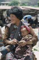 Woman in national dress or kira consisting of rectangular piece of cloth wrapped around body over a blouse or wonju held at the shoulder and waist.  Holding baby on her lap.