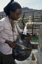 Woman filling water vessel from tap of protected spring water source.