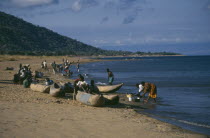 Cape Maclear with children playing on shore in wooden canoes and women washing dishes.