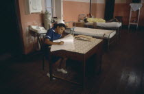 Hospital interior with nurse writing notes and patient lying on bed behind.