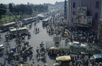 Busy street scene with crowds of pedestrians trishaws and buses.  Cinema with billboard advertising films on right.Dacca