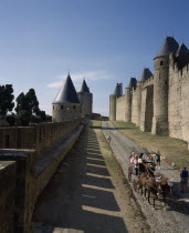 Carcassone. La Cite inner and outer ramparts with hourse drawn carriage transporting tourists along cobbled path in between