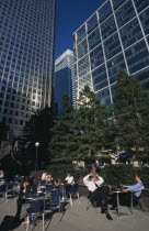 Canary Wharf.  Businessmen and women drinking at outside tables with glass fronted office buildings behind.