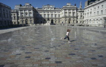 Somerset House and courtyard with rows of small fountains spouting from the ground with a girl running between them.