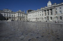 Somerset House and courtyard with rows of small fountains spouting from the ground with onlookers and visitors in the distance.