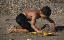 Boy on pebbly & sandy beach making a sand castle