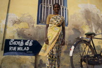 Woman in a yellow sari standing in front of a yellow wall beside a bicycle.