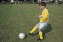Young boy kicking football.