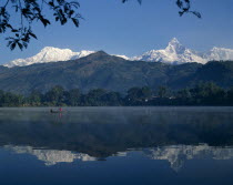 Phewa Lake with mountain peak reflected. Men in boat and branches in the foreground.