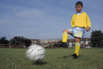 Young boy kicking football.