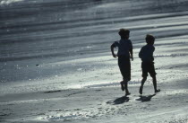 Two boys running along the wet sand of the beach