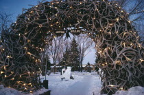 Jackson Town Square. View through Elk Horn Archway decorated with lights towards snow and a Christmas tree.