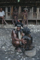 Dani Warrior man holding smoked ancestral mummy with three men sat behind him looking on