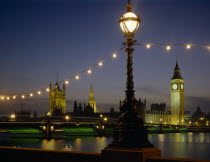 Westminster. Houses of Parliament and Westminster Bridge illuminated at night seen from across the Thames with riverside lighting in the foreground.
