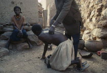 Chiropractor manipulating client in Dogon village with woman sitting at side.