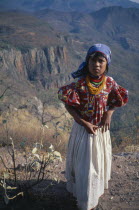 Young Huichol girl in mountain landscape.