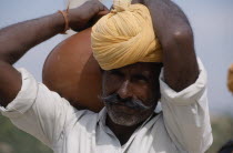 Bhansda Village.  Portrait of desert man wearing yellow turban and carrying water vessel on his shoulder.