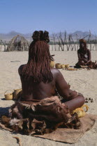 Kaokoland.  Back of seated Himba woman wearing calfskins and with her body creamed with mixture of scented butterfat and ochre to give red glow.Semi nomadic pastoral people related to the Herero and...