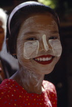 Smiling young girl wearing thanaka paste on her face in traditional Burmese style.