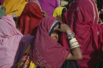 Rajasthani woman looking over her shoulder amongst crowd wearing colourful saris.